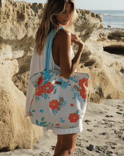 Woman holding a floral tote bag on a beach with rocky cliffs and ocean in the background