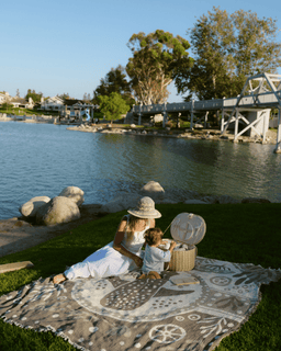 Woman and child sitting on a blanket by a lake with a scenic background