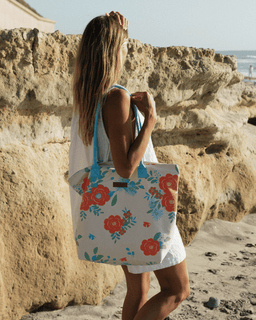 Woman holding a floral tote bag on a beach with rocky cliffs in the background
