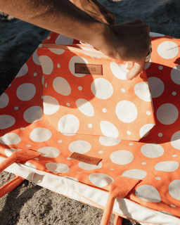 Orange and white polka dot bag with a visible brand logo on sand