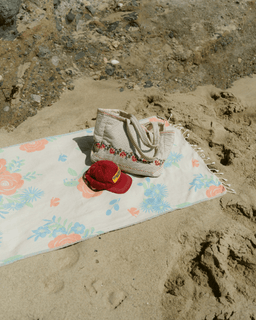 Woven bag and red cap on a floral towel in the sand