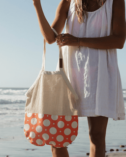 Person holding a beige bag with a red and white polka dot pattern on a beach.