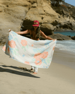 Person on a beach holding a floral towel with rocky cliffs and ocean in the background