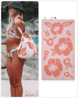 A woman on a beach wears a floral bikini and carries a matching tote bag, with a second matching towel shown flat on the right featuring large coral hibiscus flowers on a pale pink background.