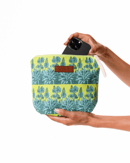 Hand holding a floral-patterned pouch with a phone case inside on a white background