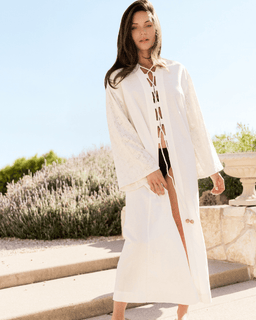 Woman in a white dress standing outdoors with greenery in the background