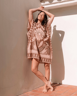 Woman wearing a patterned dress standing against a wall with sunlight casting shadows.
