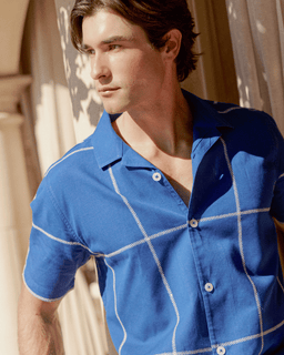 Man wearing a blue shirt with white accents in a sunlit room.