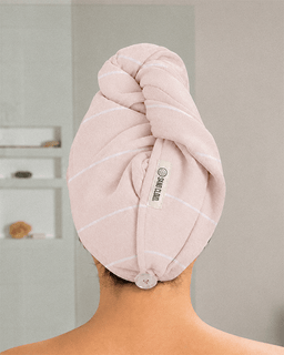 A person shown from the back wearing a light pink turban-style hair towel wrap with thin white stripes.