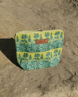 Green and yellow patterned pouch with a brand label on sand