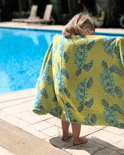 Person wrapped in a green towel with turtle pattern by a pool