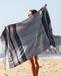 Person holding a striped beach towel on a sandy beach with ocean view