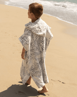 Child wearing a patterned towel on a sandy beach with ocean waves in the background