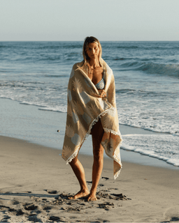 Woman wrapped in a towel on a beach with ocean waves in the background