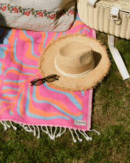 Straw hat and sunglasses on a colorful towel with a picnic basket in the background