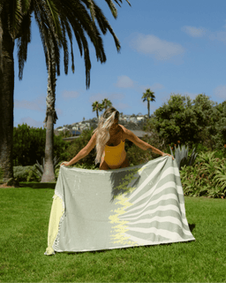 Person holding a striped towel outdoors with palm trees and greenery in the background