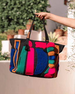 Colorful handbag with abstract patterns held by a person outdoors.