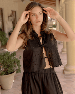 Woman wearing a black sleeveless top and skirt in an outdoor setting.
