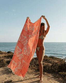 Woman holding a red patterned crab towel on a beach with ocean in the background
