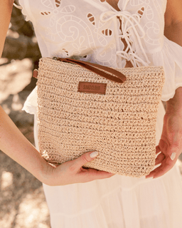 Person holding a woven clutch bag with a blurred natural background