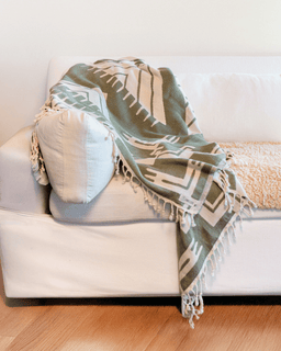 Green patterned blanket draped over a white couch with a wooden floor.