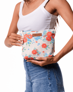 Person holding a floral-patterned pouch with a visible brand label on a white background