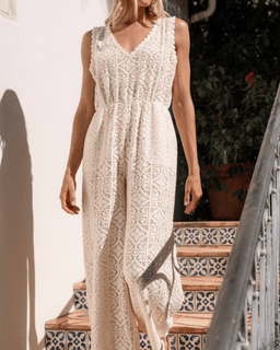 Woman wearing a white lace dress standing on a staircase with a white wall and greenery in the background.