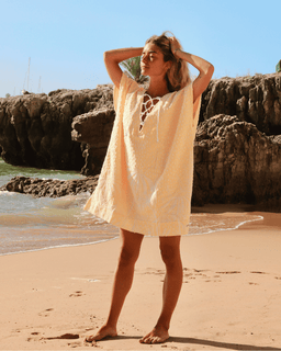 Woman in a light dress standing on a beach with rocky cliffs in the background