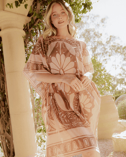 Woman wearing a patterned dress standing outdoors with greenery in the background