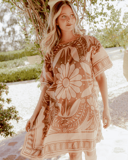 Woman wearing a floral dress standing outdoors with greenery in the background