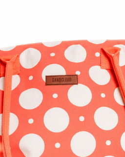 Orange tote bag with white polka dots and 'Sandcloud' brand label on a white background