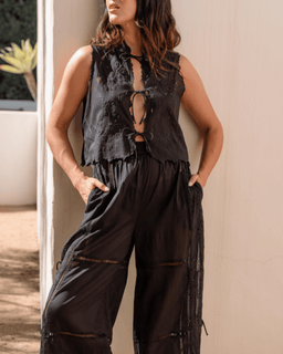 Woman wearing a black sleeveless top and pants against a beige wall.
