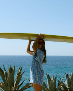 Woman holding a surfboard with a clear blue sky and ocean in the background