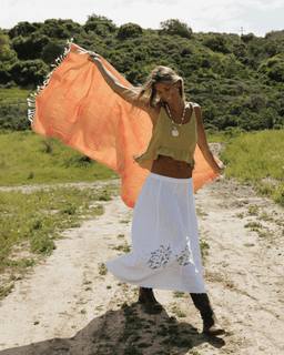 Woman holding an orange towel in a natural setting with greenery.
