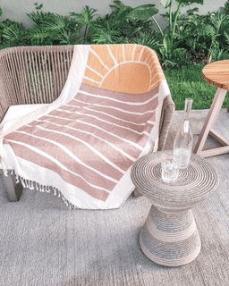 Chair with a striped towel draped over it on a patio with a side table and plants in the background.
