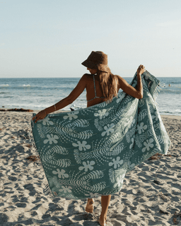 Woman on a beach holding a green floral-patterned towel