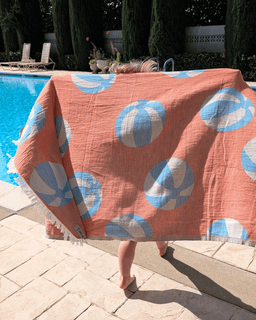 Person holding a beach towel with blue and white ball pattern near a pool