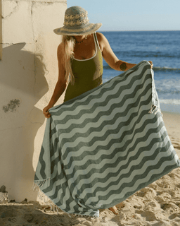 Woman on a beach holding a green and white wavy patterned towel