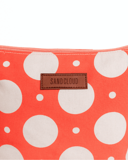 Pouch with coral and white polka dot pattern and 'Sand Cloud' brand label.