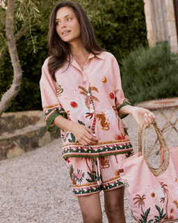 Woman wearing a pink embroidered outfit holding a matching bag outdoors.