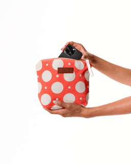 Person holding a red polka dot bag with a phone inside on a white background