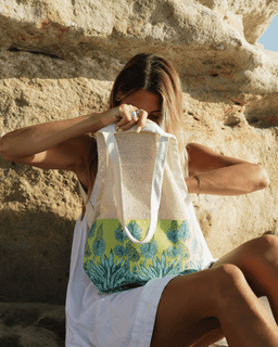 Woman holding a beach bag with a floral design against a rocky background