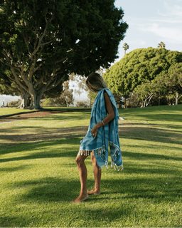 Person standing on grass wearing a blue towel with fringe details