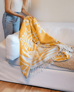 Person holding a yellow and white patterned blanket on a white couch.