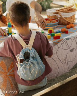 Child with a backpack playing with toys at a table outdoors