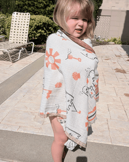Child wearing a light gray towel with orange floral patterns outdoors on a sunny day.