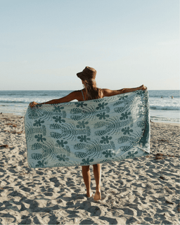 Person holding a floral-patterned towel on a beach