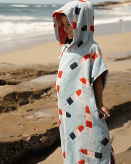 Person wrapped in a hooded towel with geometric pattern on a beach