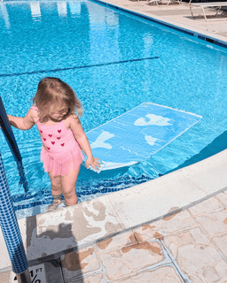 Child in a pink swimsuit standing at the edge of a pool with a blue liner.