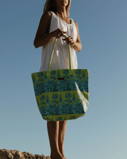 Woman holding a green and blue patterned tote bag against a clear blue sky.